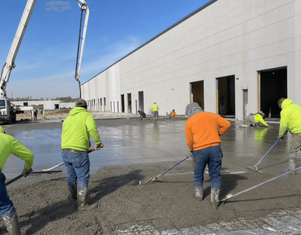 Crew finishing a large commercial concrete pour outside a warehouse building