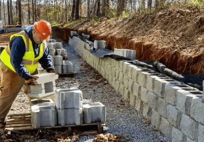 Crew building a segmental block retaining wall into a sloped, wooded lot